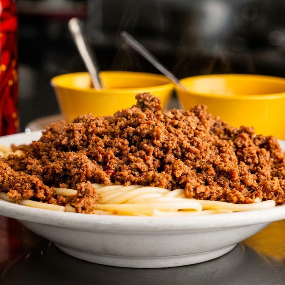 Steaming chili spaghetti with shredded cheese, yellow bowls, and pickled red peppers.
