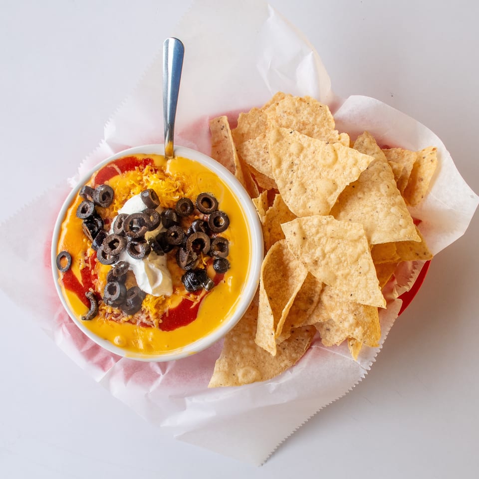 A bowl of cheesy dip with olives, sour cream, and salsa, served with tortilla chips.