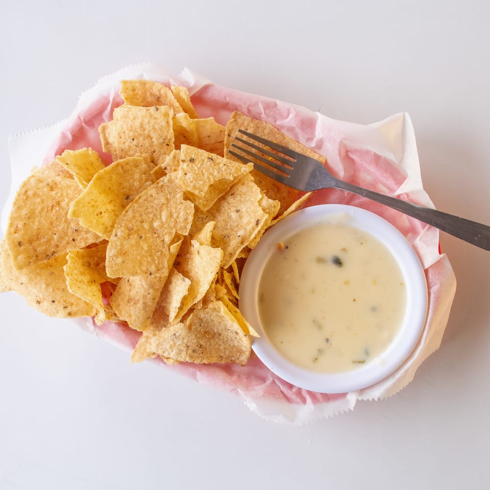 A basket of tortilla chips with a side of creamy queso dip and a fork.