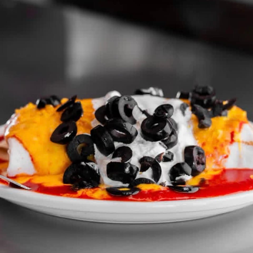 Dessert topped with whipped cream and sliced black olives, drizzled with orange and red sauces on a white plate.