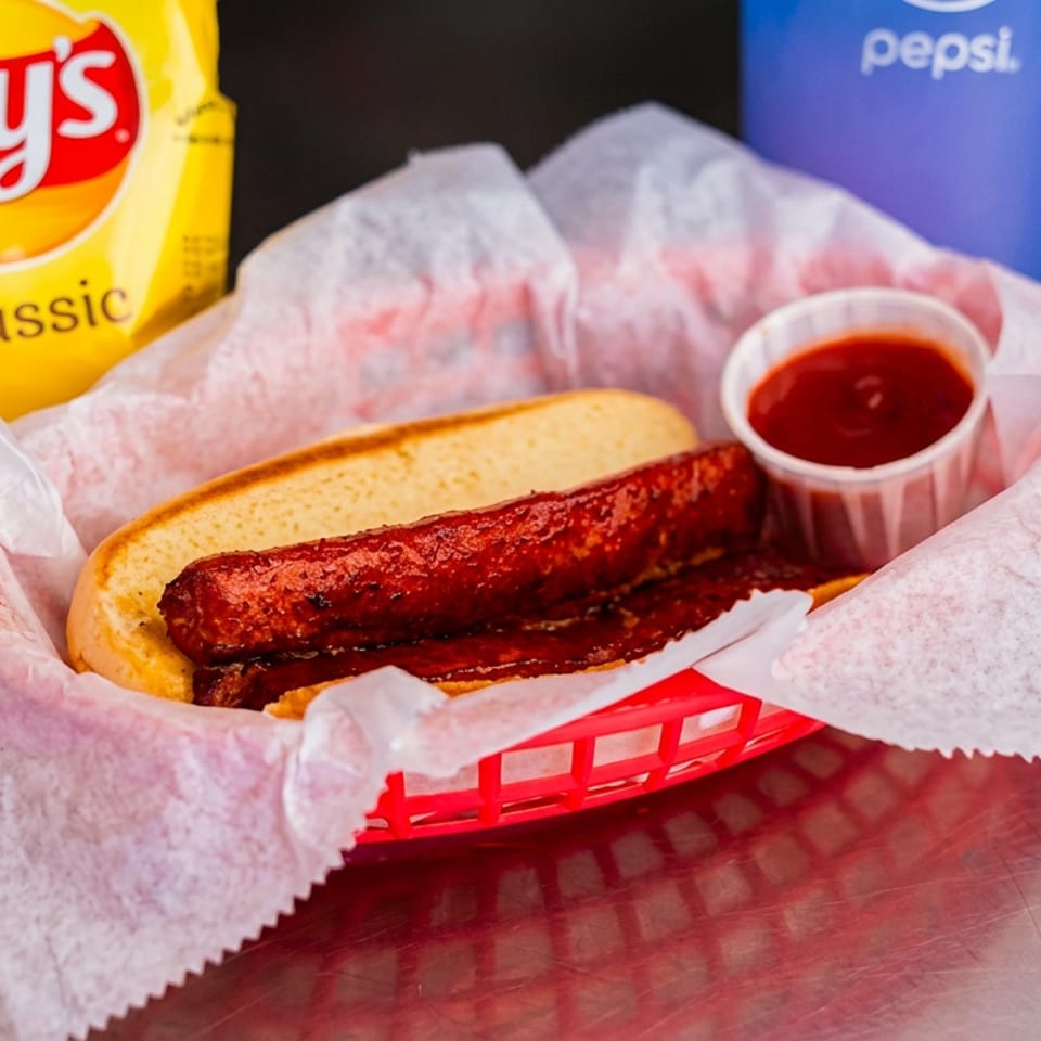 Hot dog in a red basket with ketchup, Lay's chips, and a Pepsi.